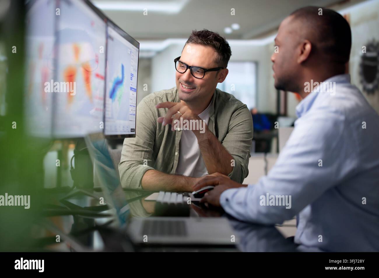 Geospatialer Analyst und Kollege arbeiten gemeinsam mit einem Laptop an der Kartierung von Hochwasserrisiken. Stockfoto