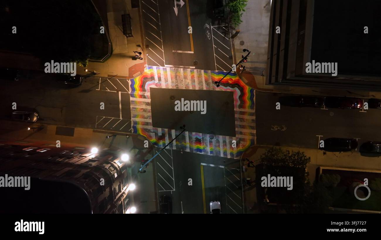 Farbiger Regenbogen auf Asphalt der Kreuzung einer amerikanischen Stadt gemalt. Auto fährt nachts auf der Straße. Laterne bei Mitternacht beleuchtet. Luftaufnahme von oben Stockfoto