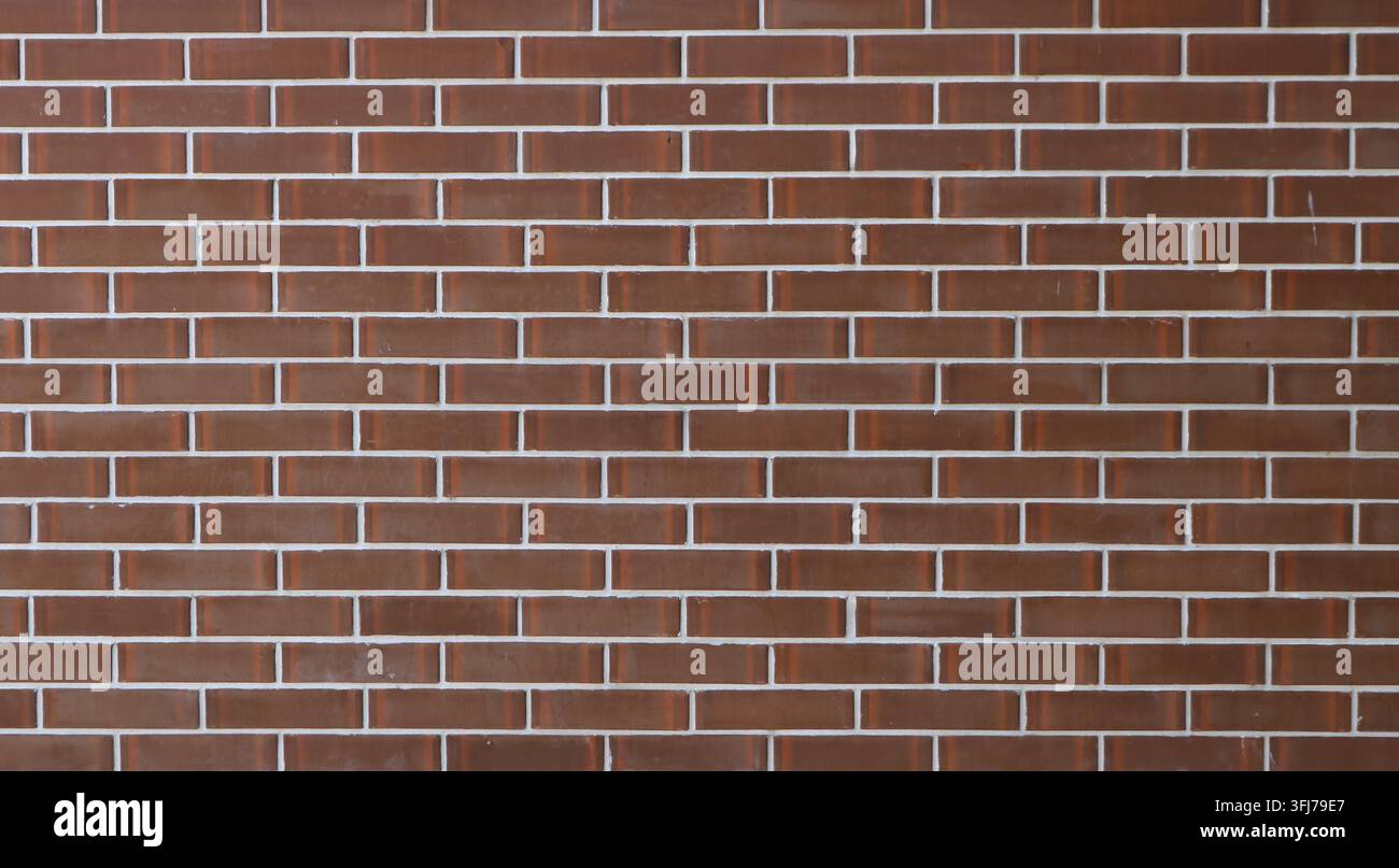 Ein Hintergrund aus neuen braunen Fliesen mit Ziegeloptik und glänzender Oberfläche. Das gleichmäßige horizontale Mauerwerk weist saubere, dünne weiße Mörtelfugen auf. Stockfoto