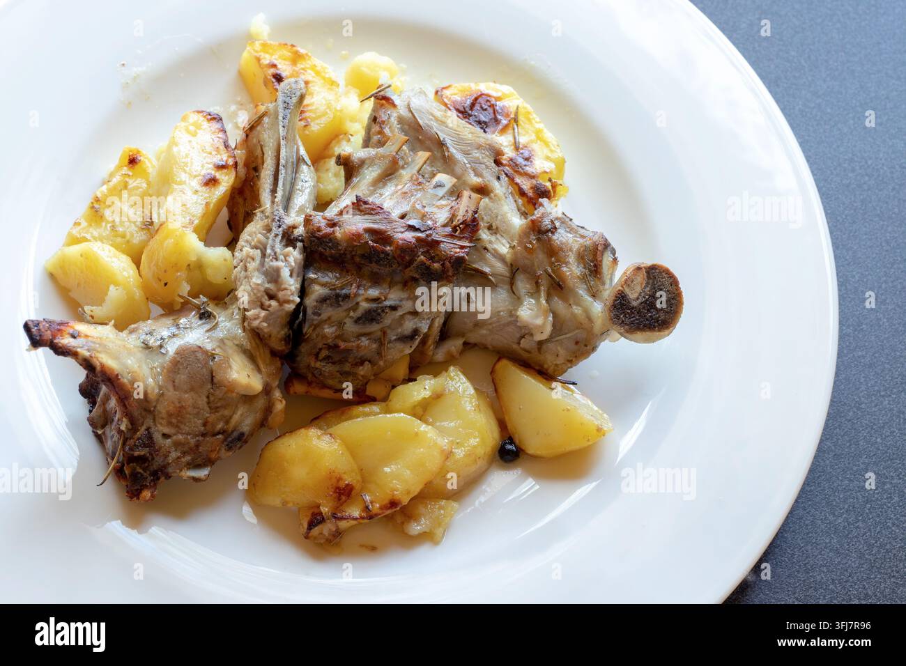 Ansicht von oben über geschultertes Lammbraten mit goldenen Röstkartoffeln, ein traditionelles italienisches ofengebackenes Fleischgericht auf einem weißen Teller Stockfoto