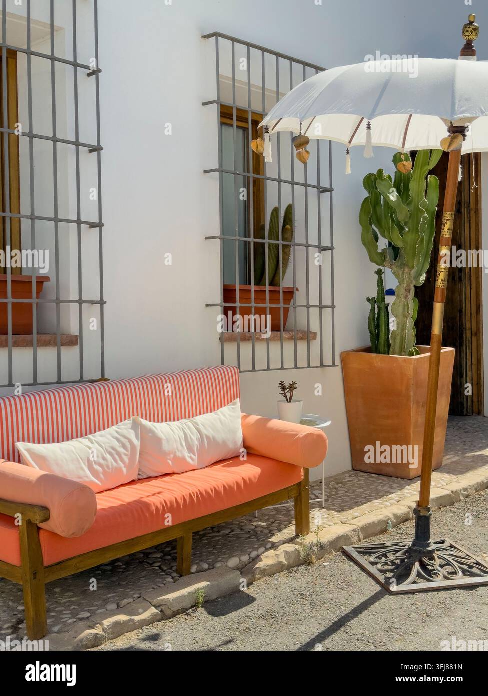 Gartenmöbel auf einer sonnigen Straße in Altea, Spanien, mit einem gestreiften Sofa mit Kissen, einem weißen Sonnenschirm, in einer sonnigen Straße. Stockfoto