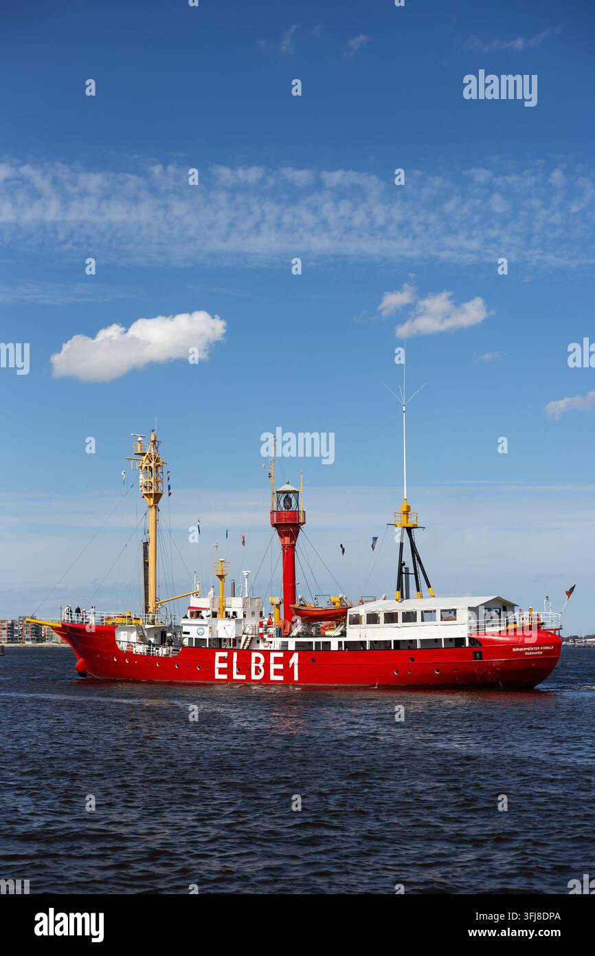 Rotes Museumsschiff Elbe 1 segelt während des Hanse Sail Festivals in Rostock unter einem hellblauen Himmel mit leichten Wolken über dem Wasser. Stockfoto
