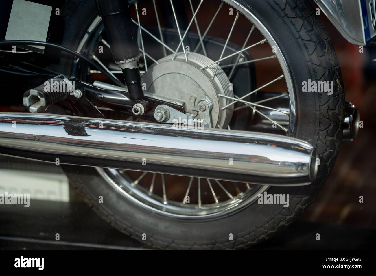 Klassisches Motorrad-Hinterrad mit Drahtspeichen, Trommelbremse und chromiertem Auspuffschalldämpfer, mechanische Komponenten für die Wartung und Teile für Oldtimer-Motorräder Stockfoto