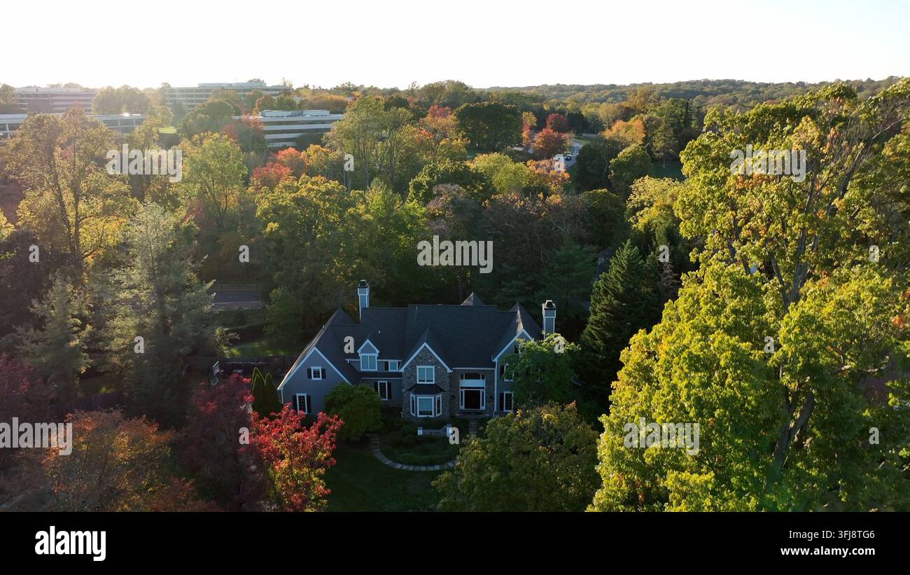 Exklusive luxuriöse Villa in den USA. Aufsteigende Luftaufnahme im Herbst mit farbenfrohem Herbstlaub an den Bäumen. Ein amerikanisches Vorstadtgeschäftszentrum kommt ins Blickfeld. Stockfoto
