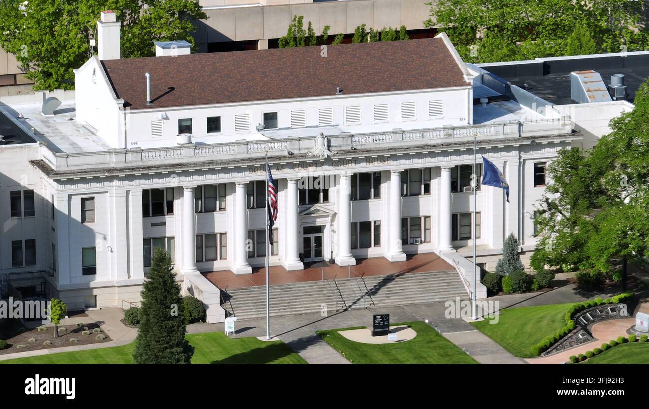 Historisches weißes Gerichtsgebäude mit Säulen, amerikanischer und oregonischer Staatsflagge, die den großen Eingangsstufen flankieren, gepflegter Rasenfläche und grünen Bäumen in der Innenstadt von Rose Stockfoto