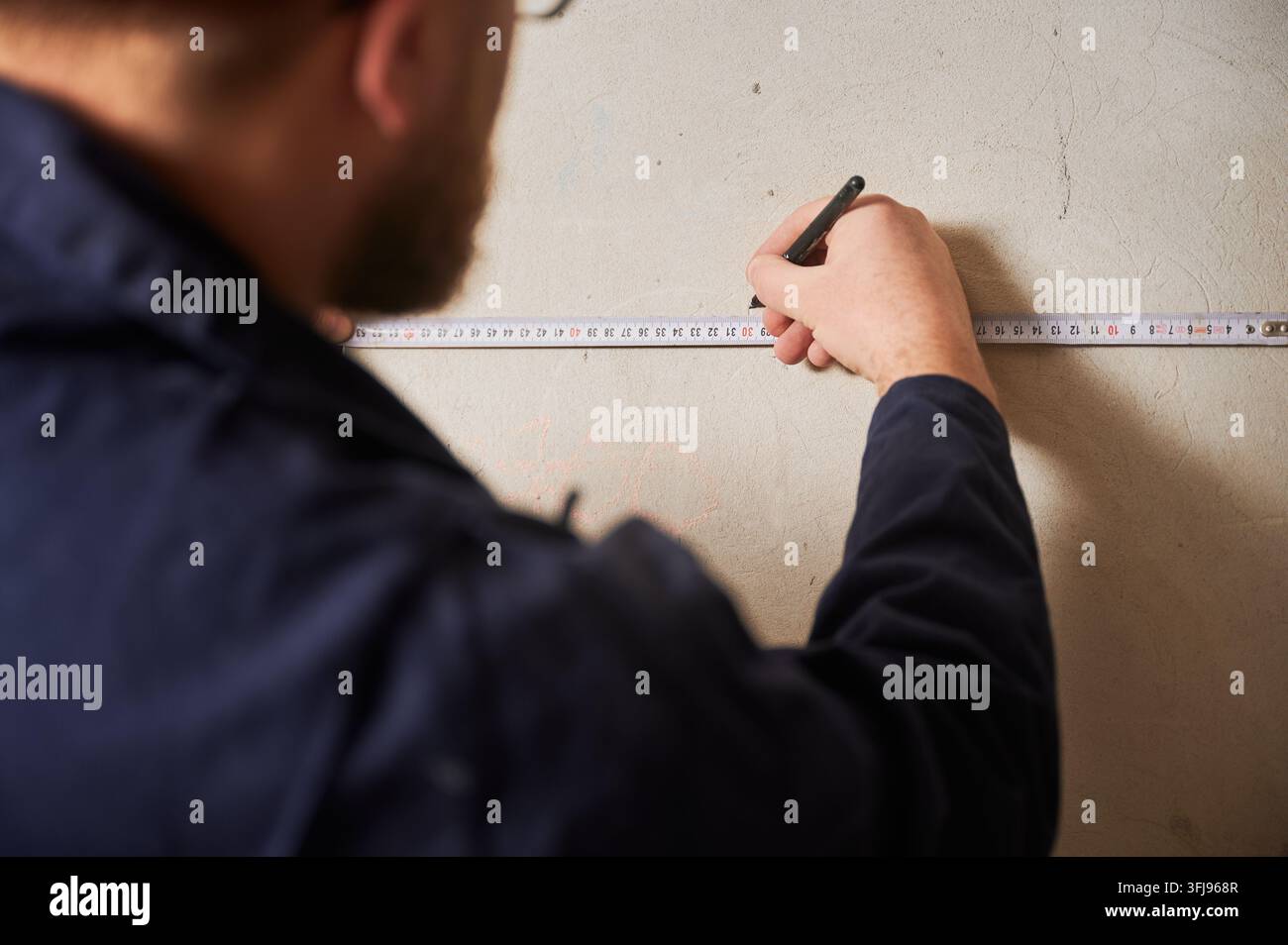 Arbeiter markiert Wandmaße mit Klebeband und Bleistift für die Installationsplanung. Nahaufnahme von Renovierungsplanung, präziser Positionierung und Konstruktionsgenauigkeit Stockfoto