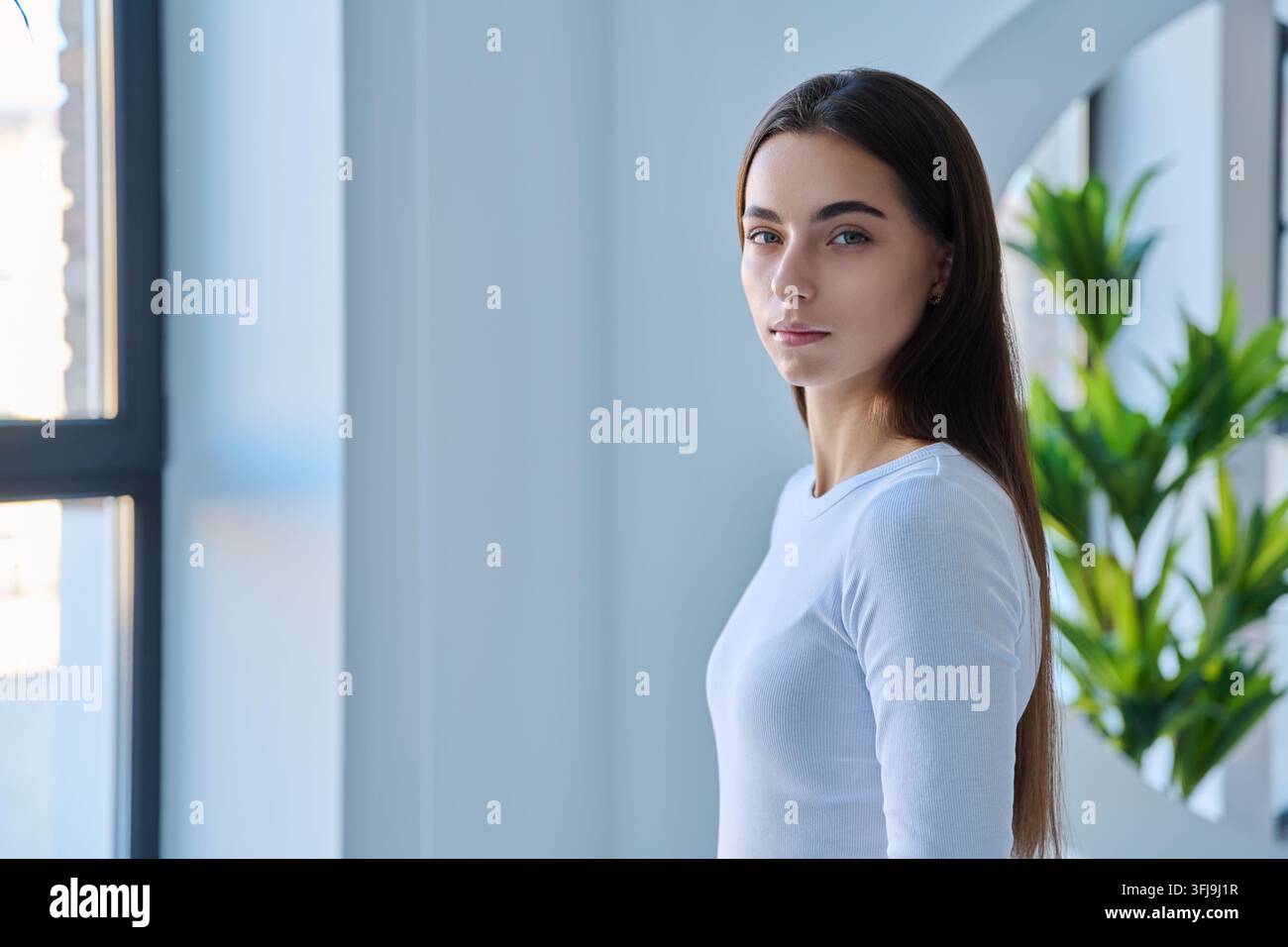 Porträt einer ernsten jungen Frau, die neben dem Fenster steht, seitliche Ansicht Stockfoto