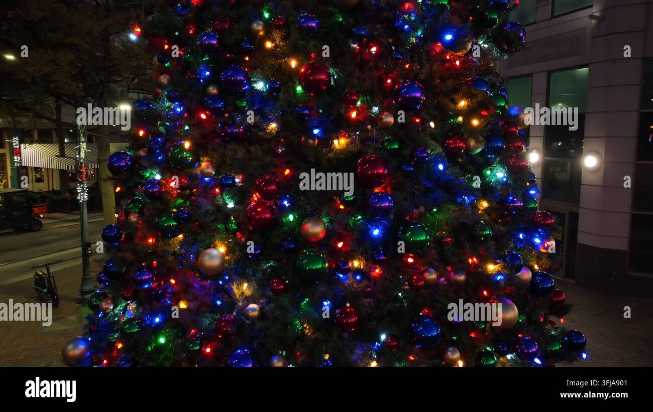 Weihnachtsbaum im Freien in der Innenstadt einer amerikanischen Stadt bei Nacht. Lichter funkeln und glänzende Ornamente. Steigender Luftorbit, Memphis, Tennessee. Stockfoto