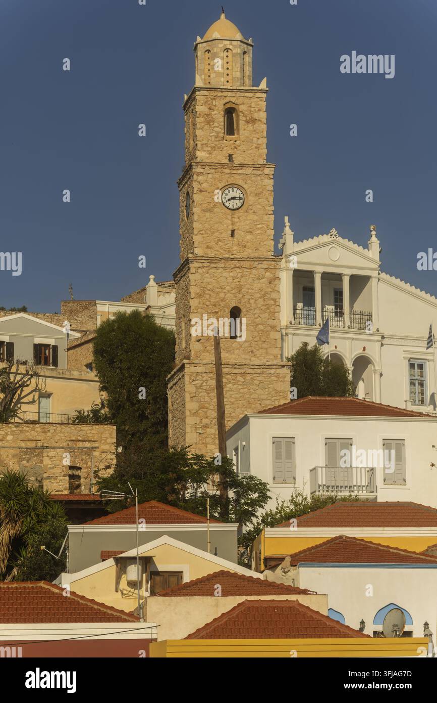 Der Uhrturm und das Rathaus erheben sich über roten Dächern und weißen Wänden, ihre steinerne Form hebt sich vom klaren Himmel und dem warmen Insellicht ab. Stockfoto
