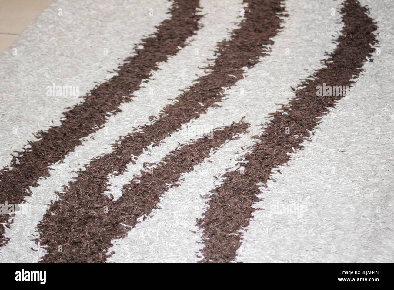 Makroaufnahme eines weichen, zotteligen Teppichs mit einem gestreiften Muster in Creme- und Brauntönen und einer plüschigen, texturierten Oberfläche. Stockfoto