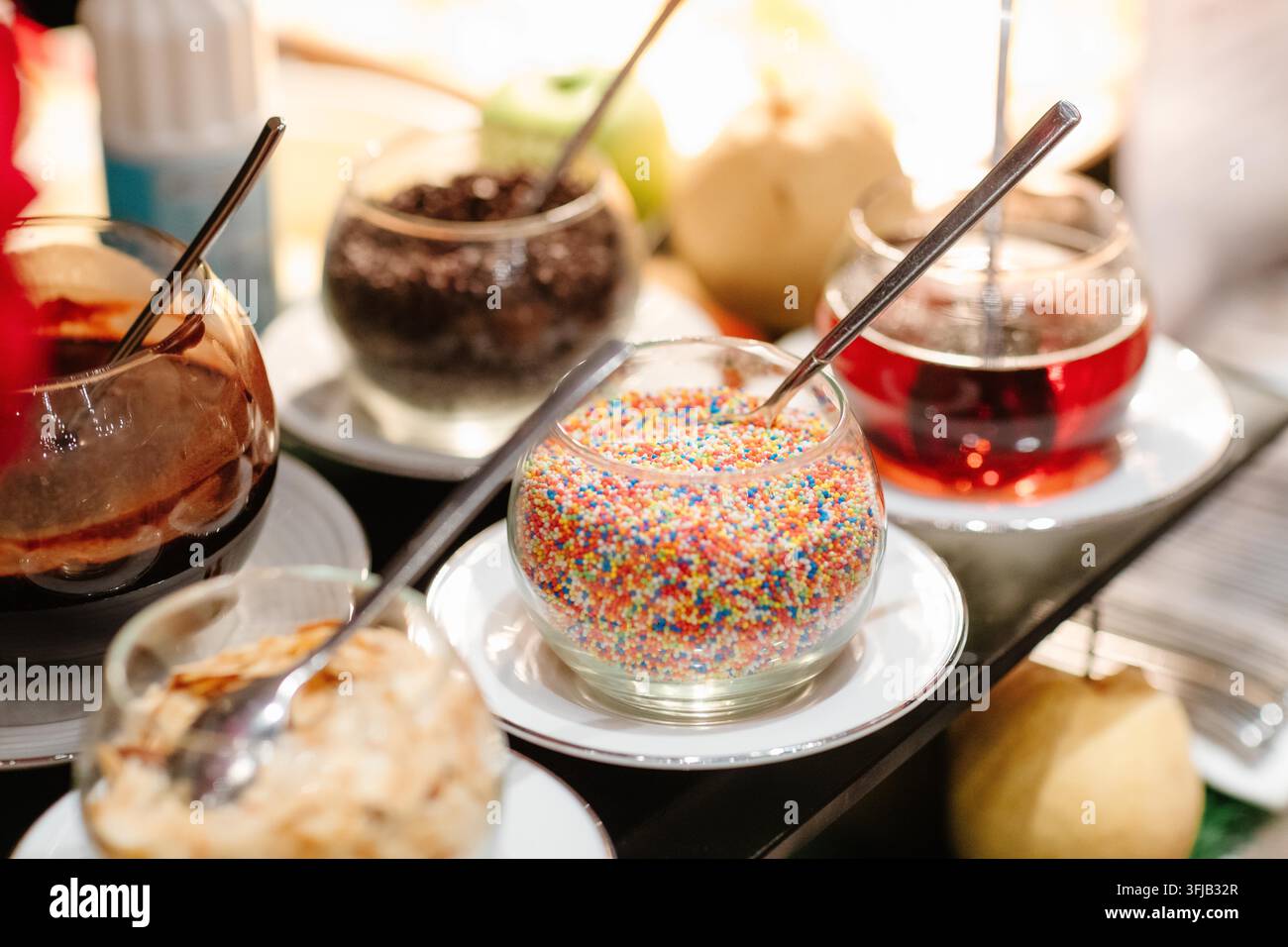 Verschiedene Dessertbeläge, Streuseln und süße Soßen in Glasschalen auf einem Buffet-Tisch Stockfoto