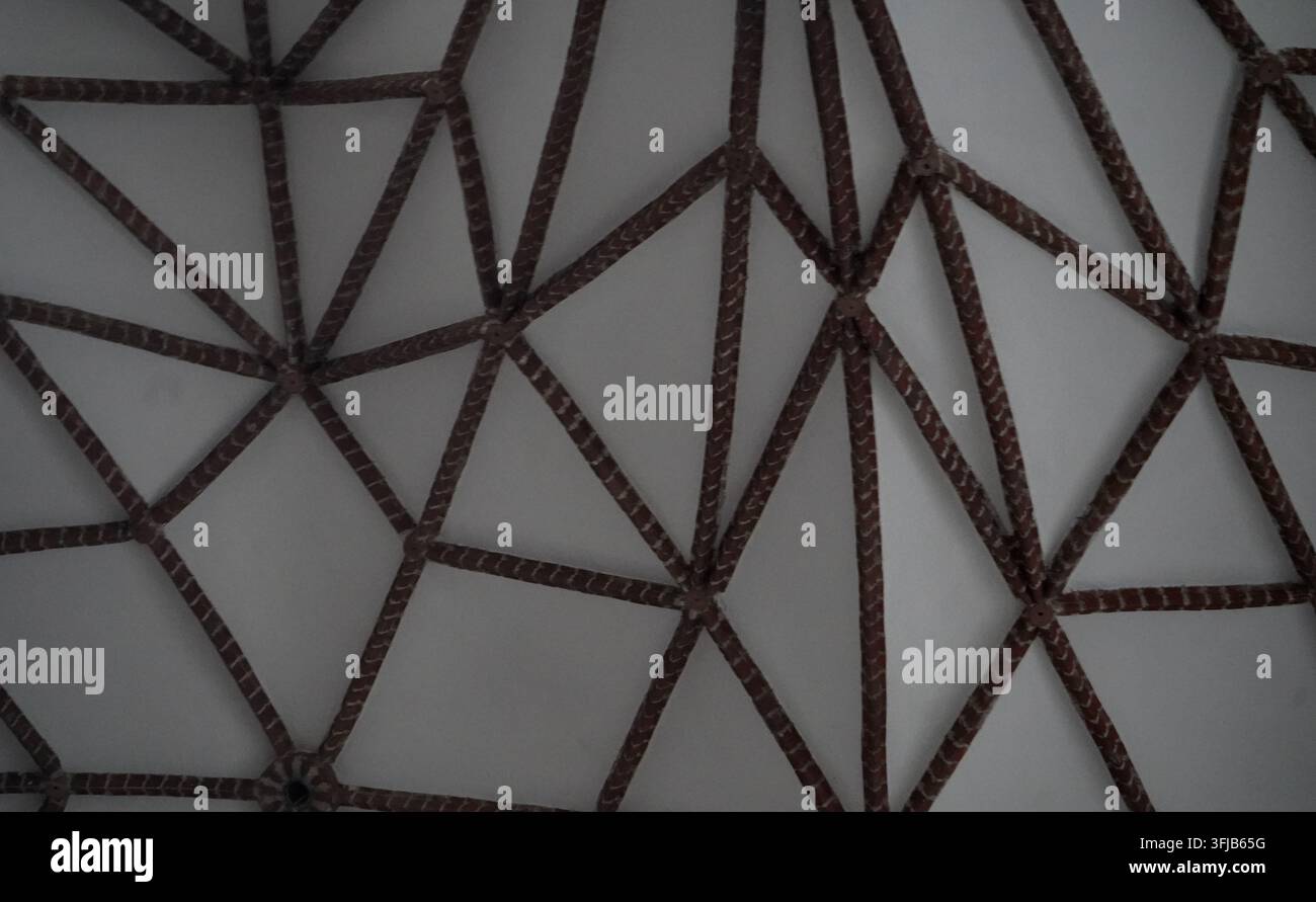 Abstraktes geometrisches Muster aus miteinander verbundenen dunklen Holzbalken, das dreieckige Formen an einer weißen Gip Decke erzeugt. Stockfoto
