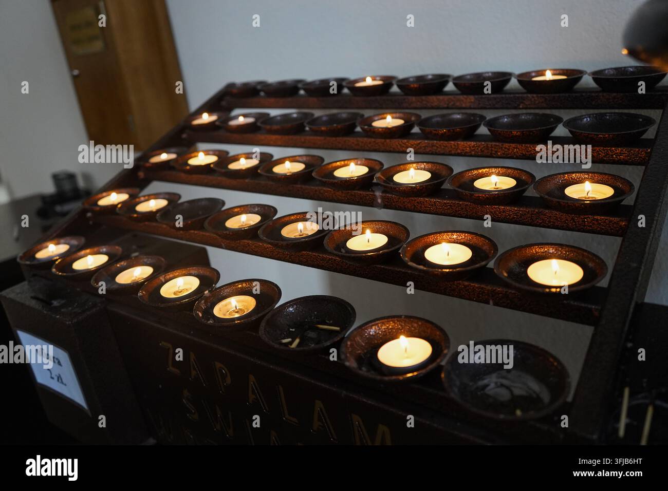 Reihen brennender Votivkerzen, die in dunklen Keramikschalen in einer Kirche für Gebet, Meditation und spirituelle Erinnerung platziert wurden. Stockfoto