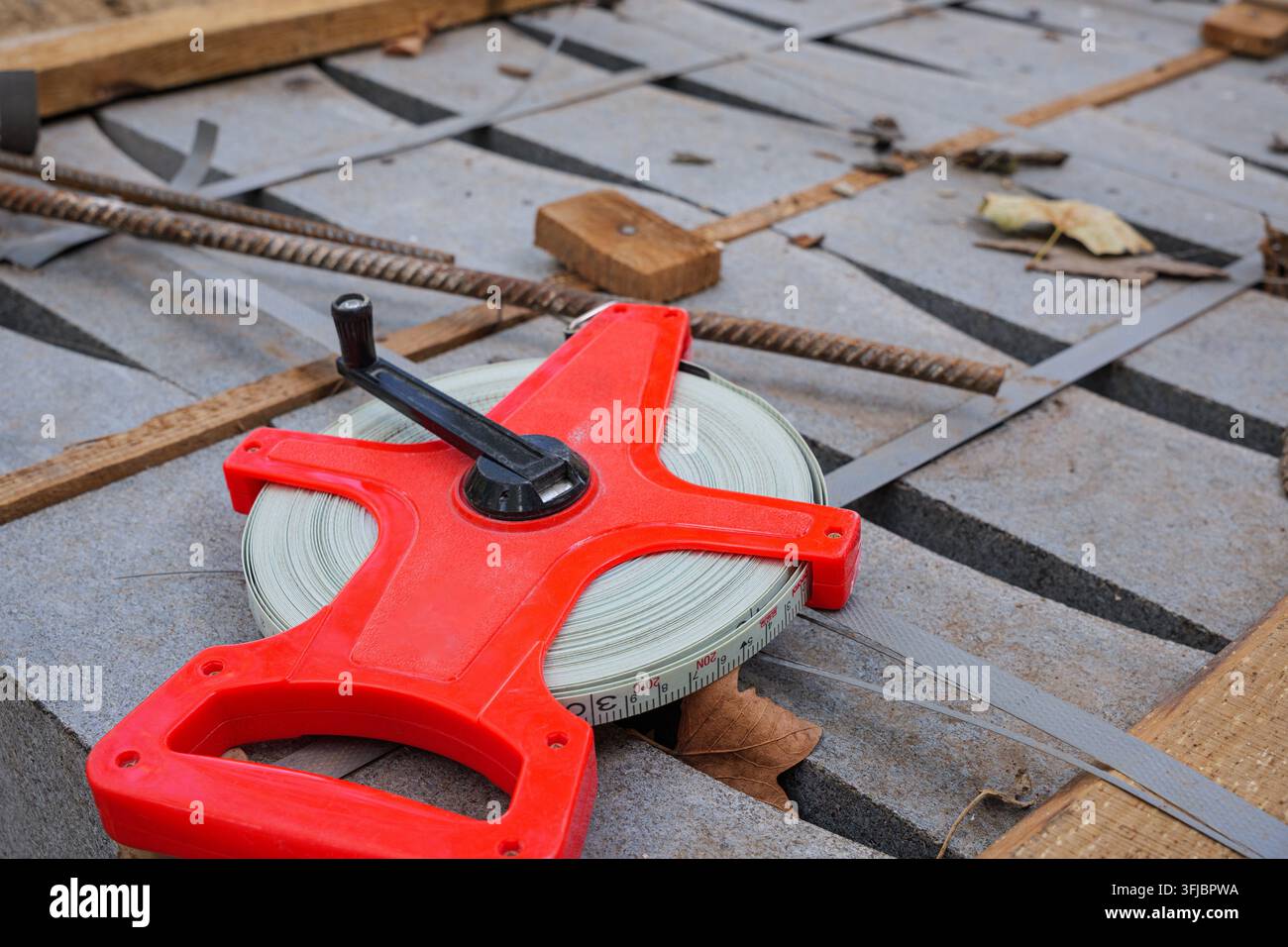 Eine Hochwinkel-Nahaufnahme einer roten langen Maßbandrolle, die auf gestapelten Betonpflasterplatten an einer Baustelle im Freien während des Tages liegt. Stockfoto