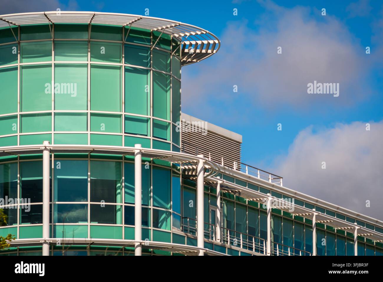 Modernes Glas-Bürogebäude mit einer gebogenen, grün getönten Fassade und Stahlsäulen, das Himmel und Wolken reflektiert. Corporate Business Architektur vermittelt p Stockfoto