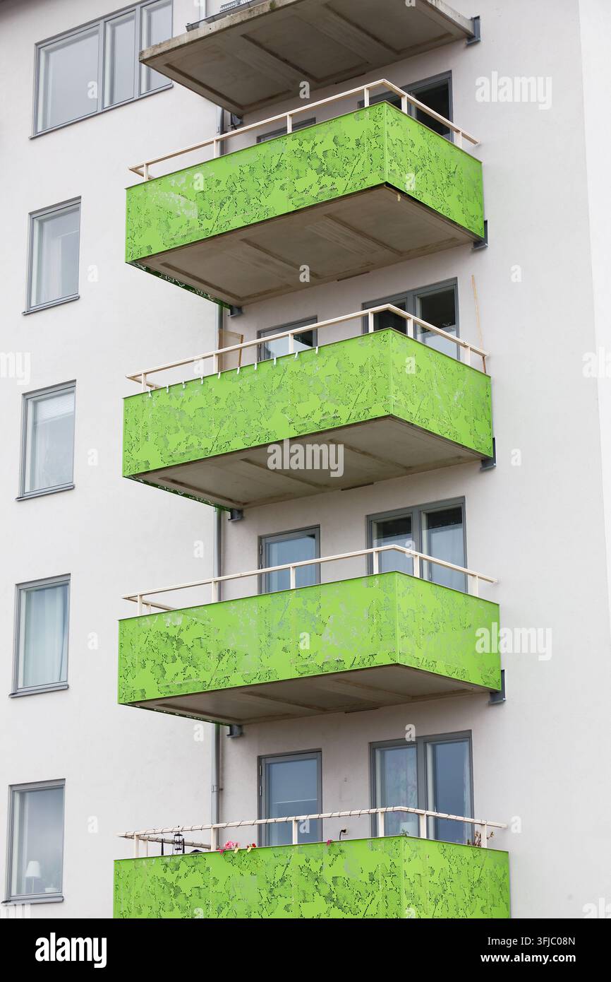 Moderne Wohnhausfassade mit markanten limettengrünen perforierten Metallbalkonen, weißen Außenwänden und mehreren Wohnfenstern. Contem Stockfoto