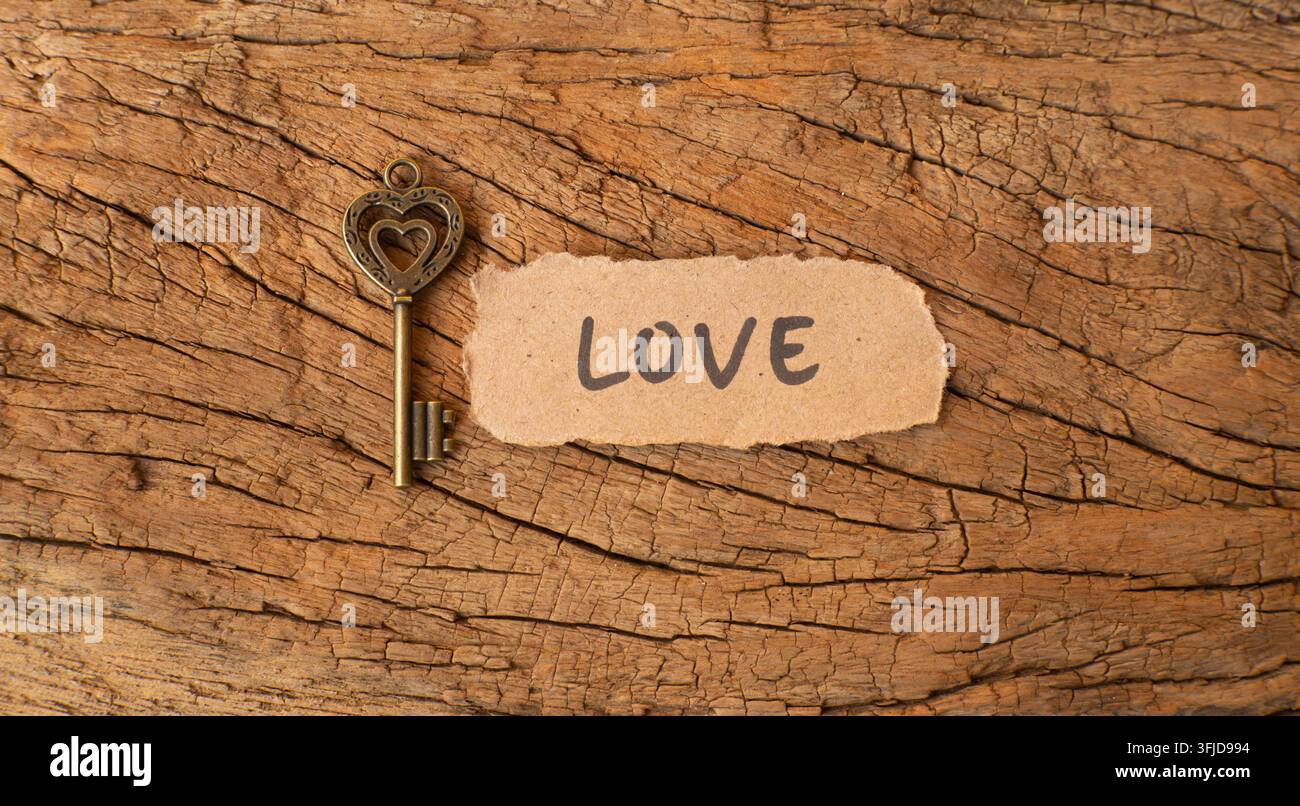 Antiker Skelettschlüssel mit Liebespapier-Etikett auf rustikalem Baumarbeitshintergrund, symbolisiert Liebe, Vertrauen, bedeutungsvolle Beziehungen Stockfoto
