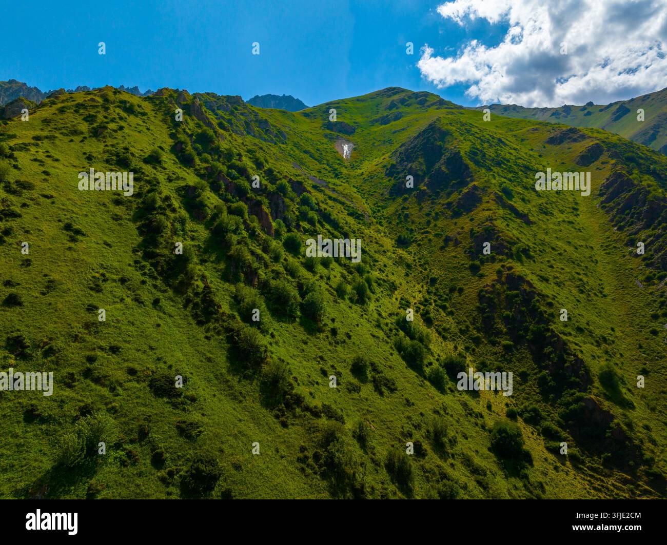 Grüner Berghang unter einem strahlend blauen Himmel mit vereinzelten Wolken und Iron Seep auf dem Berghang. Stockfoto