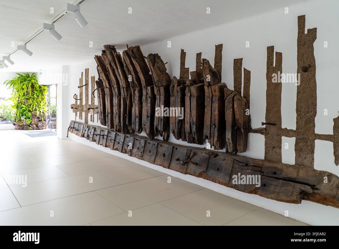 Eine künstlerische Wandinstallation aus gealtertem Holz schmückt einen hellen, gefliesten Innenraum in Lanzarote. Das natürliche Licht betont die Textur Stockfoto