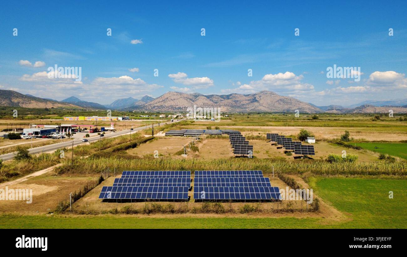 Luftbild einer Solarzellenanordnung, die auf einem ländlichen Feld installiert wurde, mit Bergen und blauem Himmel im Hintergrund, Konzept der erneuerbaren Energie. Stockfoto