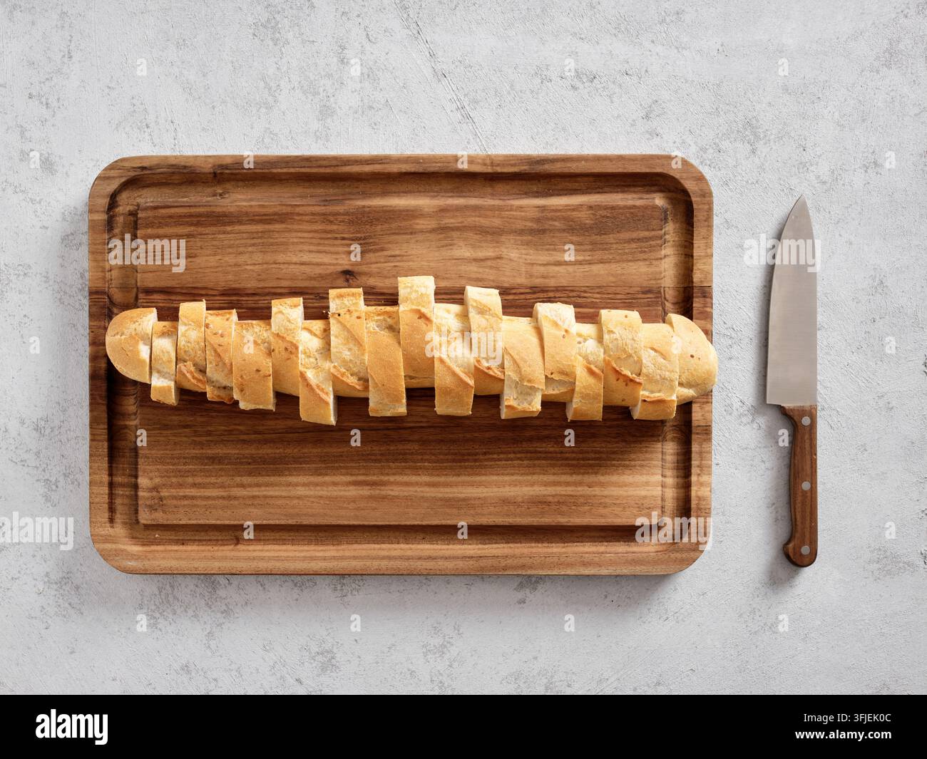 Frisch gebackenes Baguettebrot in kleinere Stücke geschnitten, das auf einem rustikalen Holzbrett mit einem Messer daneben liegt Stockfoto