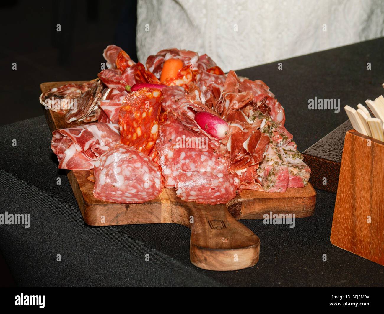 Fleischwaren aus der Fleischerei auf einem Holzschneidebrett auf einem schwarzen Tisch angeordnet. Stockfoto
