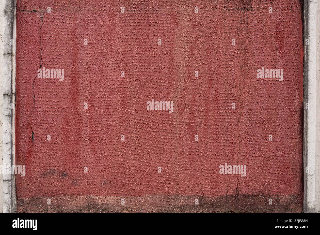 Strukturierte Wand, bedeckt mit verwittertem rotem Putz, wodurch eine gealterte architektonische Oberfläche für Grunge-, Bau- und Hintergrundkonzepte entsteht. Stockfoto