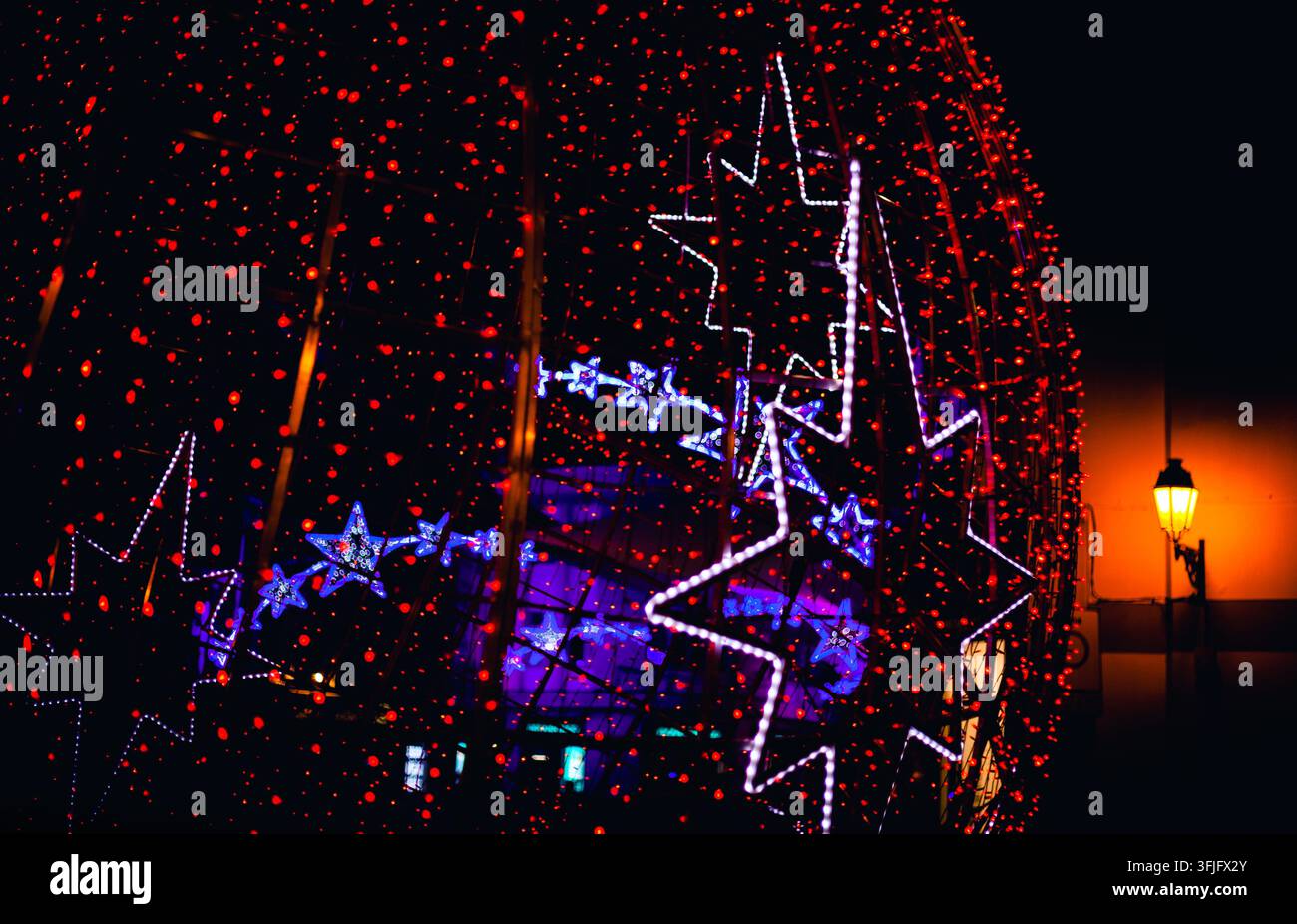 Nahaufnahme von leuchtenden festlichen Weihnachtslichtern mit großen beleuchteten Sternen und roten Lichterketten während der Nacht. Stockfoto