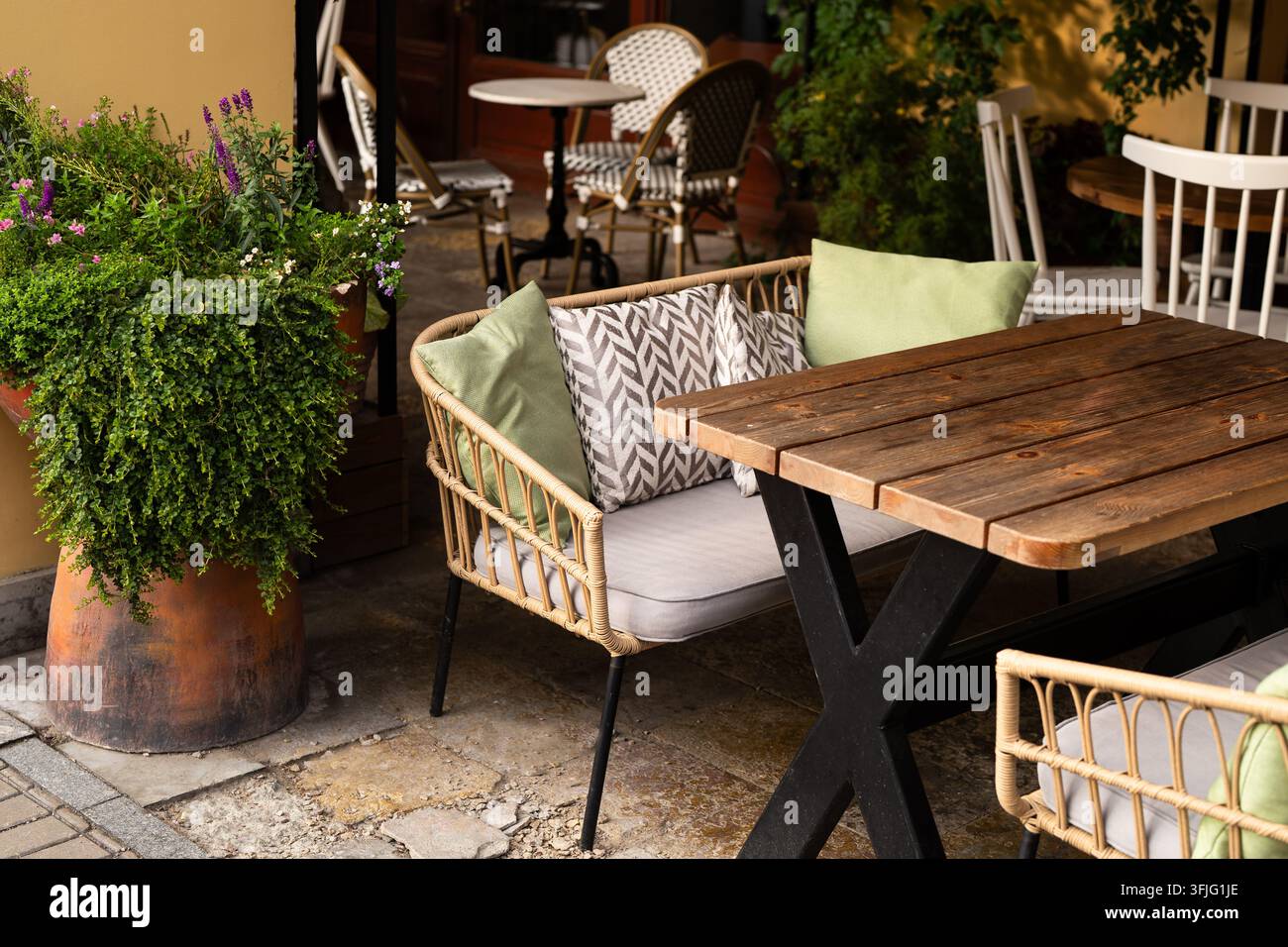 Außenbereiche von Restaurants mit gemütlichem Sofa, Holztisch und dekorativer Blumenpflanze im Topf. Stockfoto