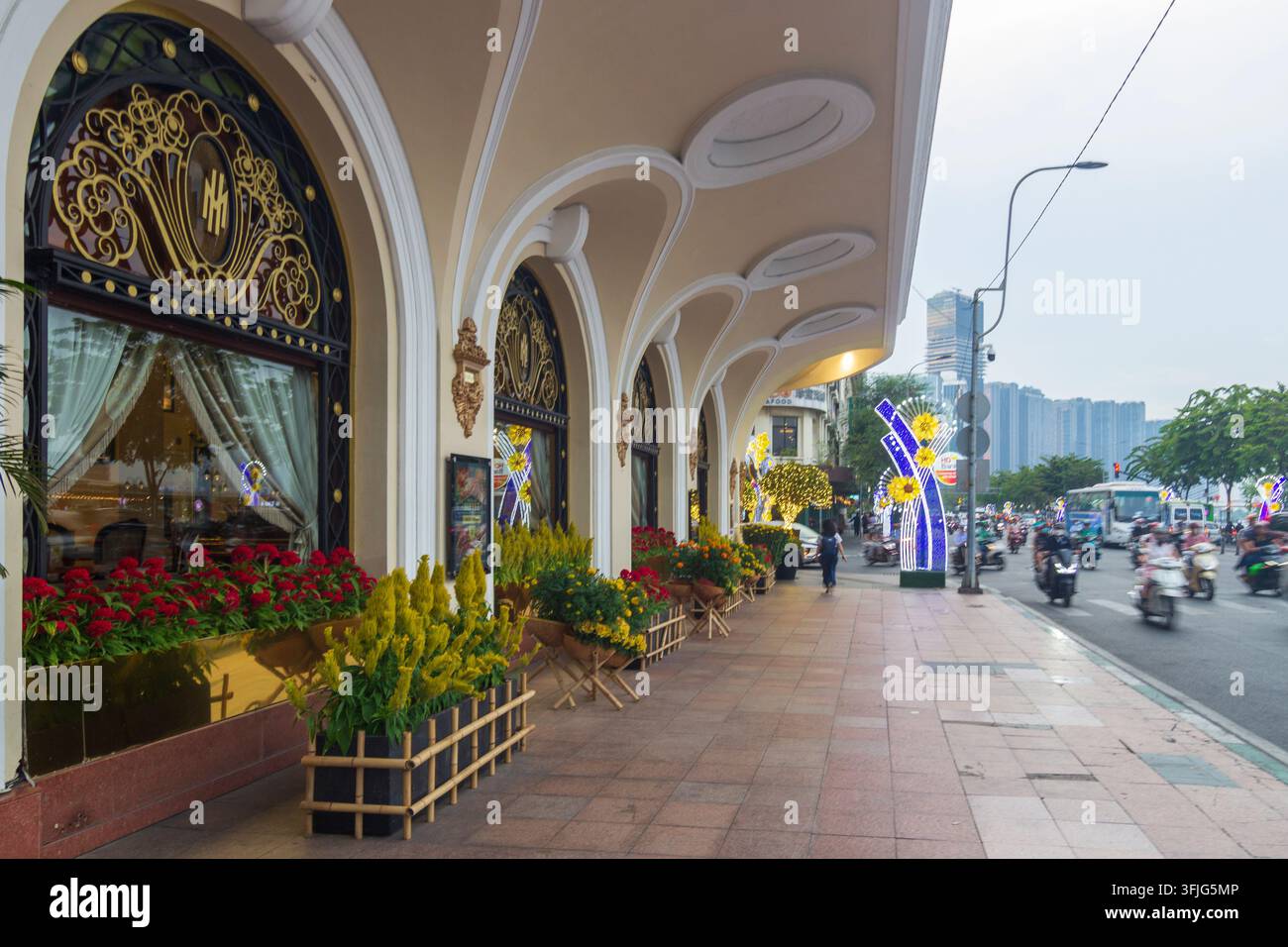 Reflektierendes Schaufensterglas erzeugt eine geschichtete Sicht auf eine verzierte Gebäudefassade mit gewölbten Fenstern, goldener Eisenarbeit, Blumenkästen und einem städtischen Bürgersteig. Stockfoto