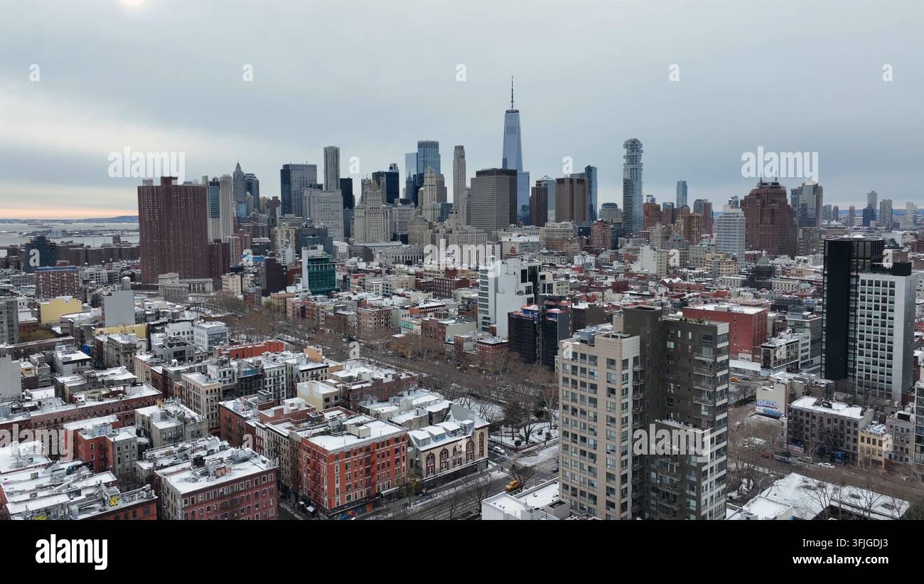 Vorortbezirk von New York City mit schneebedeckten Dächern und berühmter Manhattan-Skyline mit modernem One World Trade Center im Hintergrund. Bewölkter Winter Stockfoto