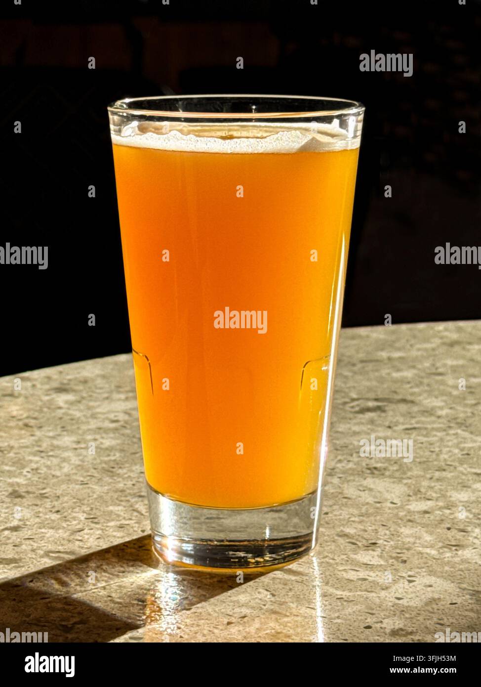 Pint amberfarbener Biere auf einem Tisch in einer Bar, die von Sonnenlicht durch ein Fenster hinterleuchtet wird. Keine Menschen. Kopierraum. - Smartphone-aufgenommenes Stockfoto
