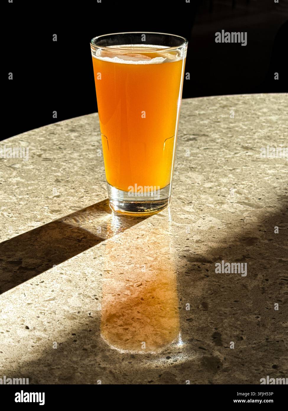 Pint amberfarbener Biere auf einem Tisch in einer Bar, die von Sonnenlicht durch ein Fenster hinterleuchtet wird. Keine Menschen. Kopierraum. - Smartphone-aufgenommenes Stockfoto