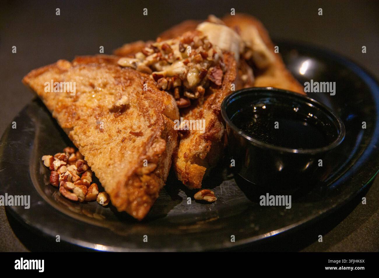 Eine Nahaufnahme, horizontal aufgenommen, zeigt ein herzhaftes Frühstücksgericht mit goldbraunen French-Toast-Dreiecken, die mit Bananenscheiben und Crus garniert sind Stockfoto