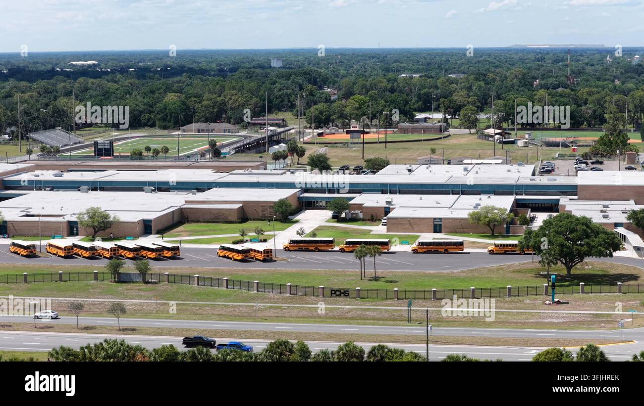 PCHS-Buchstaben markieren den Umgrenzungszaun außerhalb der High School in Plant City, Florida, eine Reihe geparkter gelber Busse säumt den Parkplatz, während Autos an der Straße neben dem Baseballplatz vorbeifahren Stockfoto