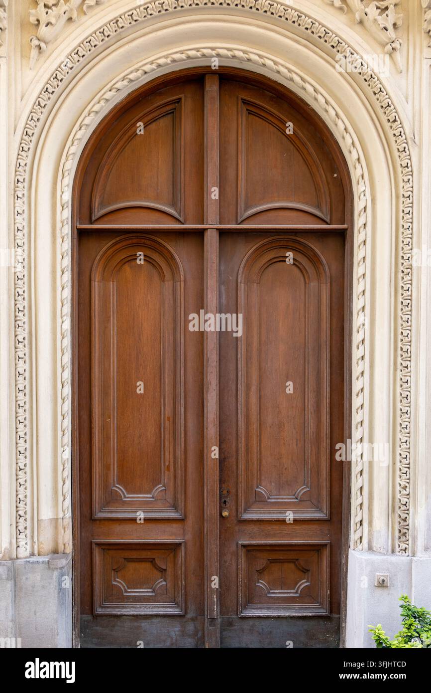 Eine verzierte hölzerne Doppeltür steht in einem geschnitzten Steinbogen an der Fassade eines Gebäudes. Stockfoto