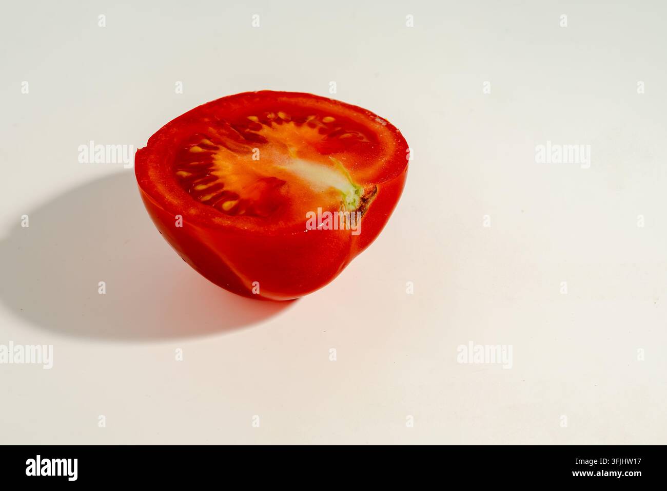 Nahaufnahme einer halbierten reifen roten Tomate auf sauberem weißem Hintergrund mit sichtbaren Samen, saftigem Inneren, glänzender Schale und weichem natürlichem Schatten Stockfoto