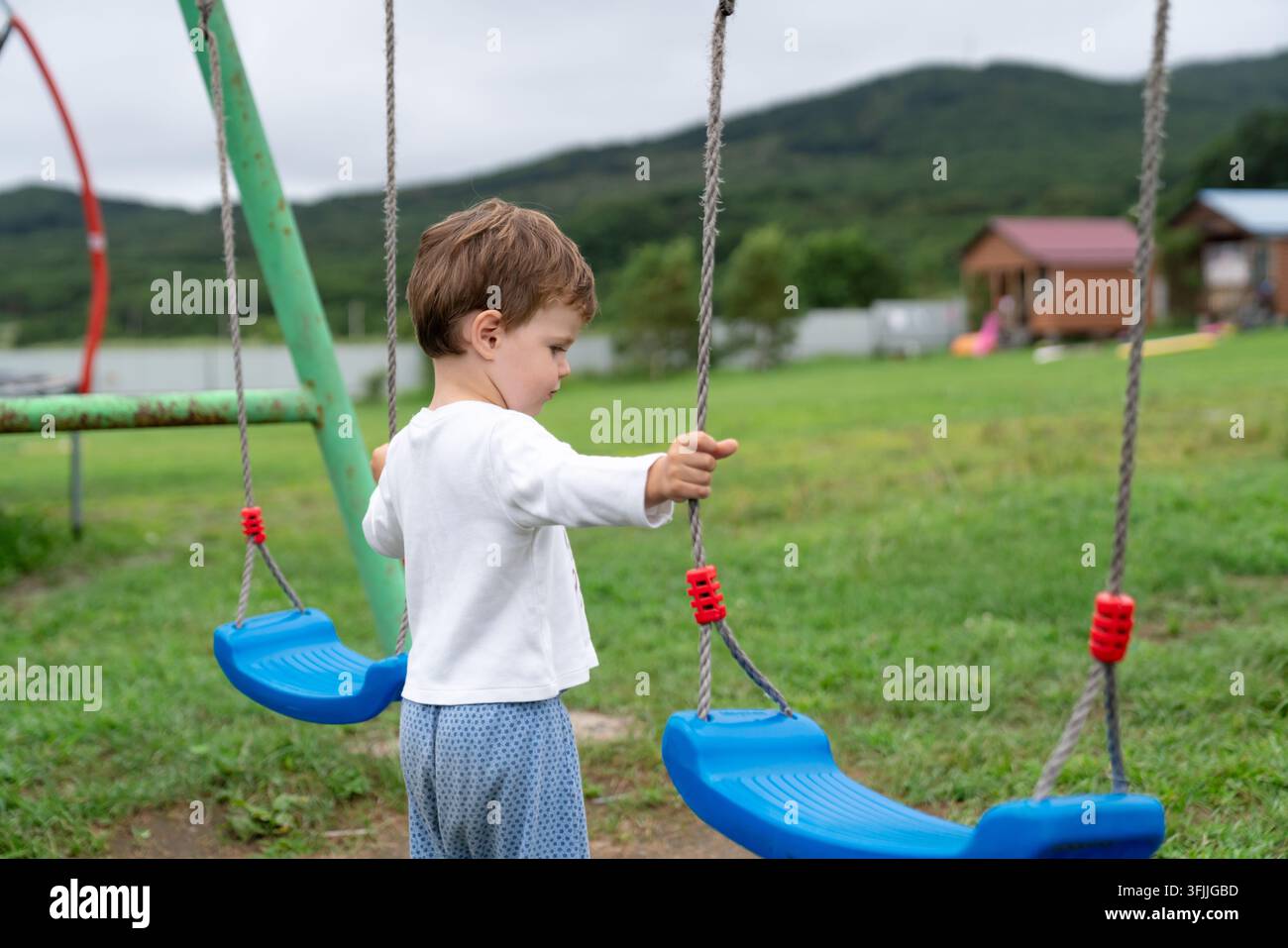 Kind hält Schaukelseile auf dem Sommer-Spielplatz und fängt einen authentischen alltäglichen ruhigen Moment der Kindheit ein Stockfoto