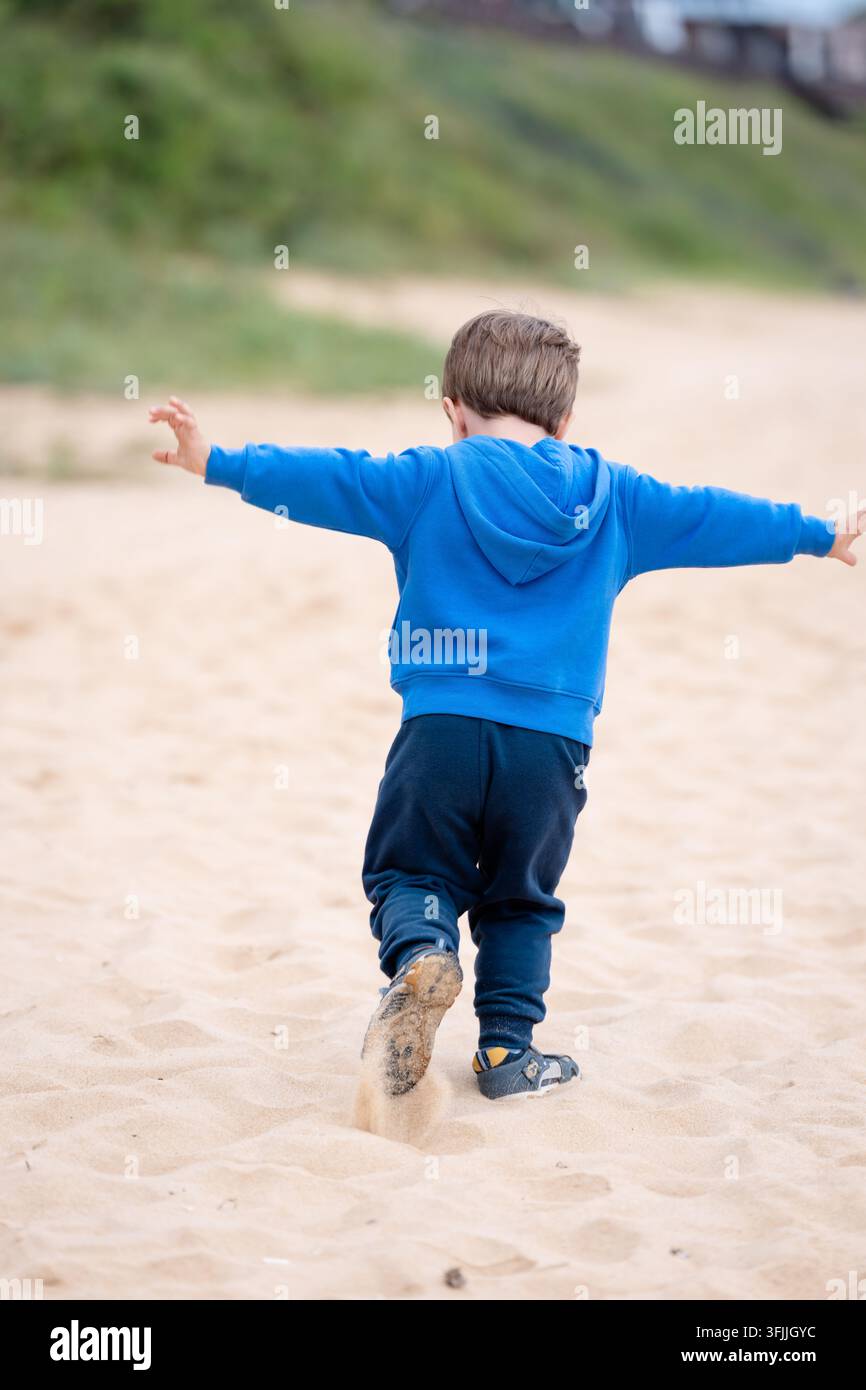 Kind, das auf sandigem Boden geht, und authentische alltägliche Bewegung und einfache unbeschwerte Sommerkindheit einfängt Stockfoto