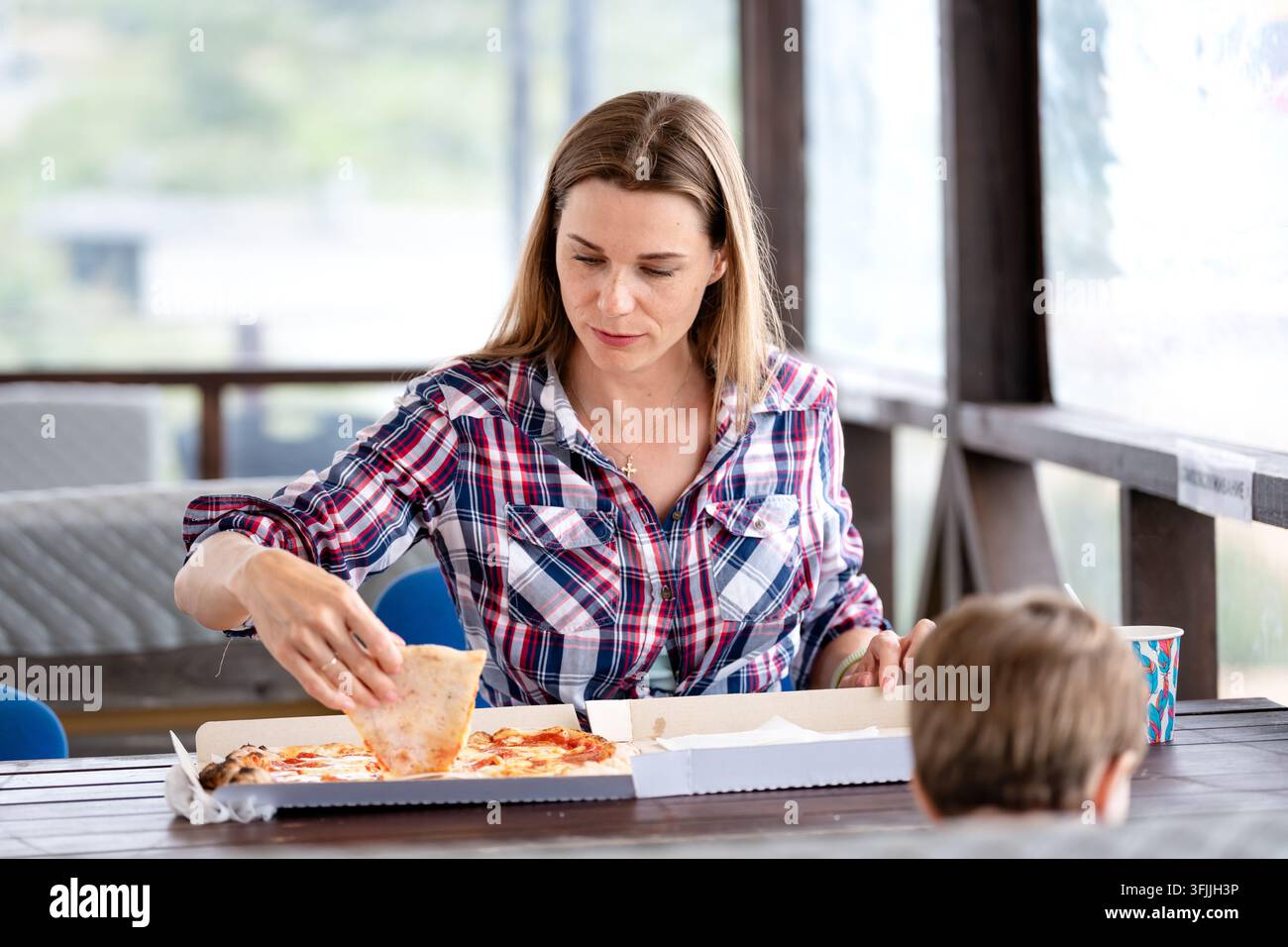 Mutter und Kind teilen Pizza am Tisch und fangen authentische alltägliche Wärme und einen einfachen Familienmoment ein Stockfoto