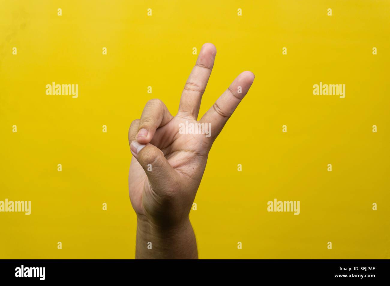 Eine männliche Hand zeigt klare Zwei-Finger-Grüße, die Friedenszeichen darstellen, vor einem lebhaften gelben Hintergrund, Zeige- und Mittelfinger sind ausgestreckt Stockfoto