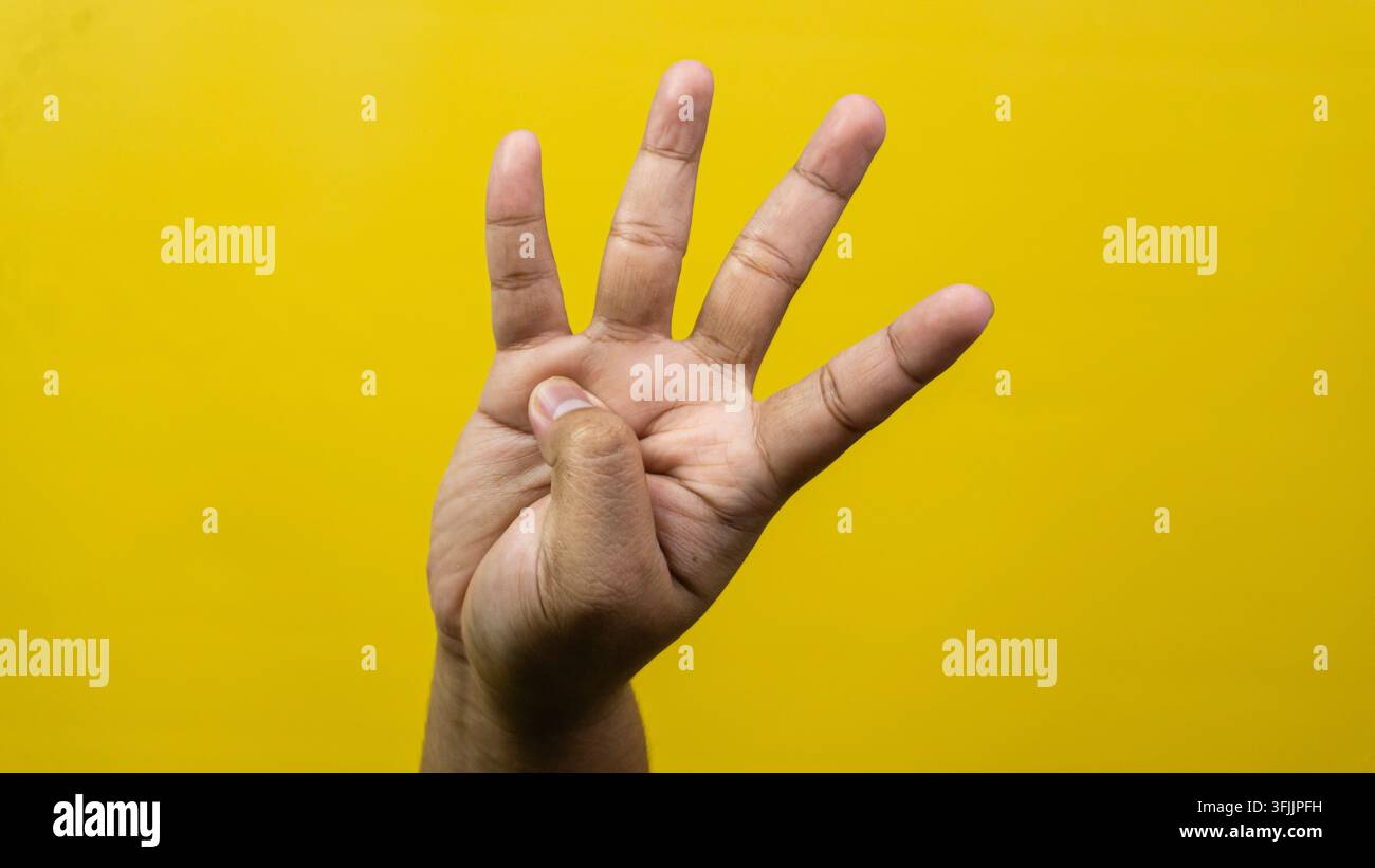 Eine männliche Hand zeigt deutlich vier ausgestreckte Finger vor einem hellgelben Hintergrund, der Daumen legt sich über den Handflächen nach innen, sodass die verbleibenden Ziffern poi Stockfoto