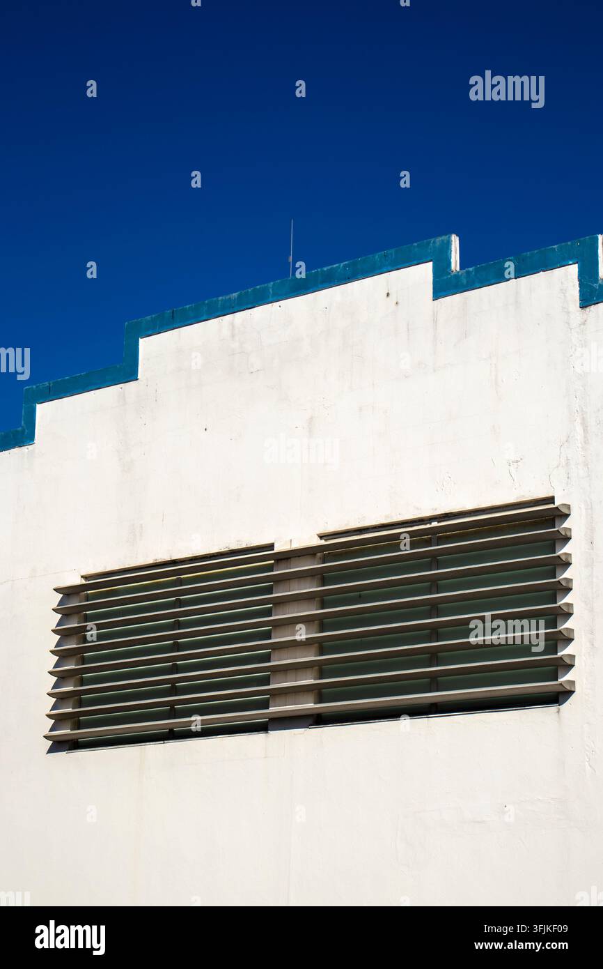Geometrische weiße Gebäudewand mit horizontalen Lamellen, klaren Linien und einem auffälligen tiefblauen Himmelshintergrund, aufgenommen im sonnigen Brasilien. Stockfoto