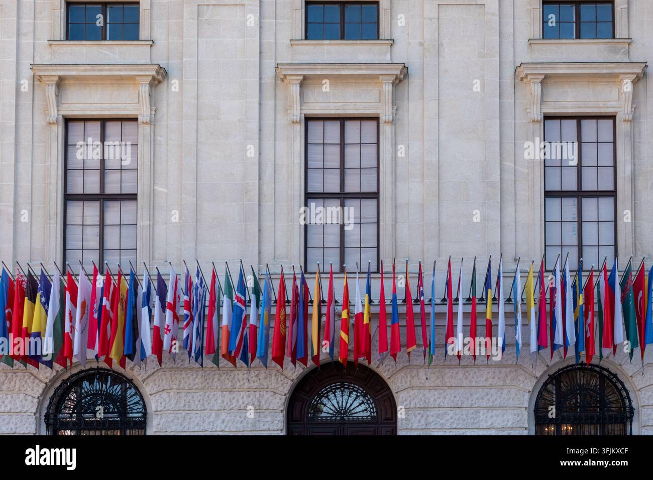 Viele internationale Flaggen hängen über der Fassade eines eleganten historischen Gebäudes. Stockfoto