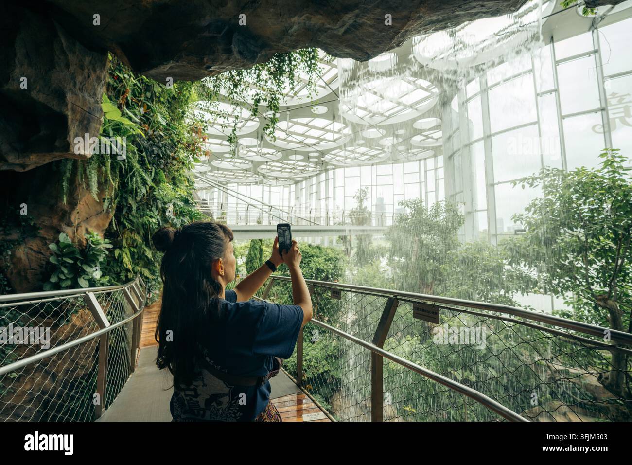 Shanghai, 11. August 2026: Ein Besucher fotografiert den üppigen Indoor-Wasserfall im Shanghai-Gewächshausgarten Stockfoto