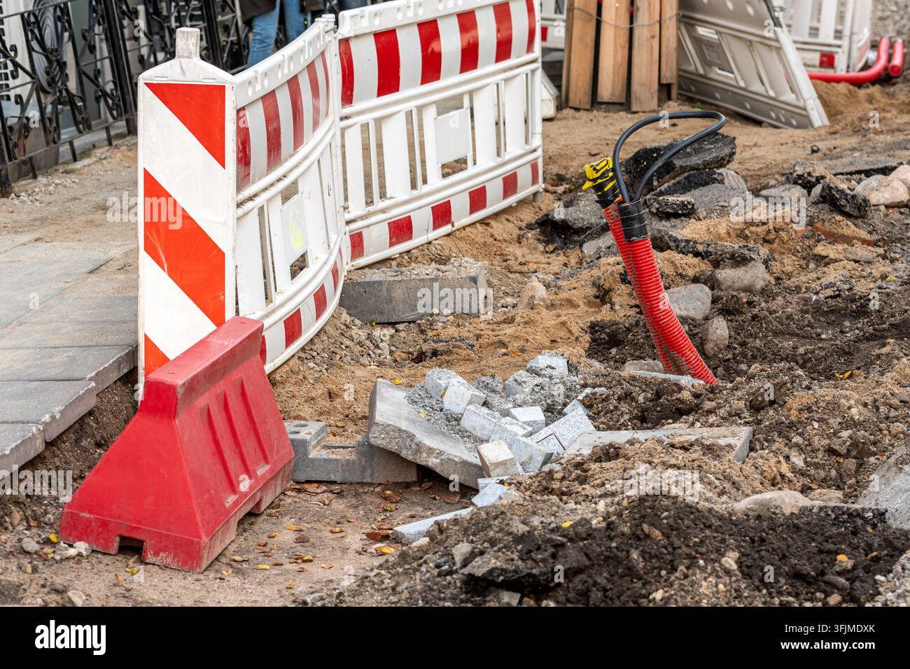 Bauarbeiten im Gange, abgegrenzt durch rot-weiße Sicherheitsbarrieren und Barrikaden, mit einem Aushubgebiet und loser Erde neben der Fahrbahn Stockfoto