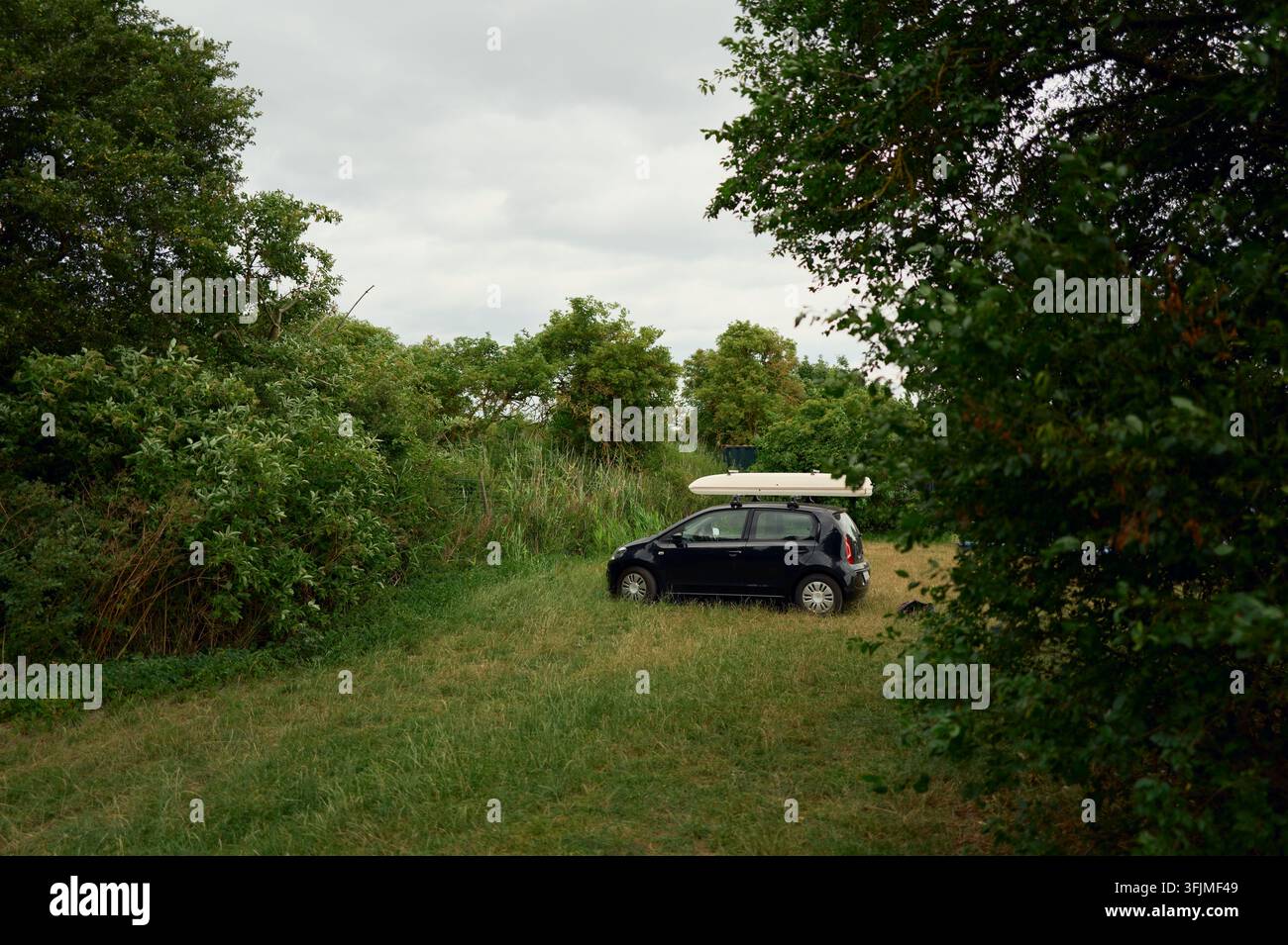 Kleines schwarzes Auto mit Dachkoffer auf einem Feld geparkt Stockfoto