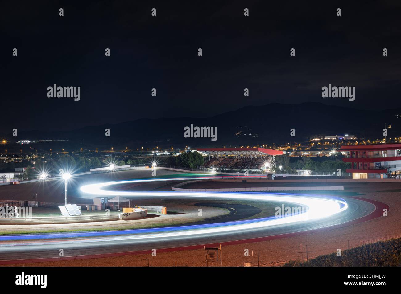 Langzeitbelichtung Nachtansicht von Lichtspuren, die S-Kurven auf einer Rennstrecke mit Flutlicht und Bergsilhouette im Hintergrund bilden. Stockfoto