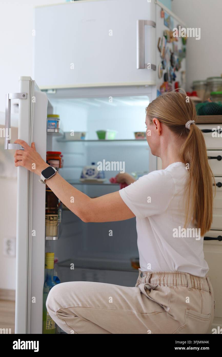 Frau wählt Zutaten aus einem Kühlschrank, ideal für Inhalte über Lebensmitteleinkäufe, Ernährung und gesunde Mahlzeitvorbereitung. Stockfoto