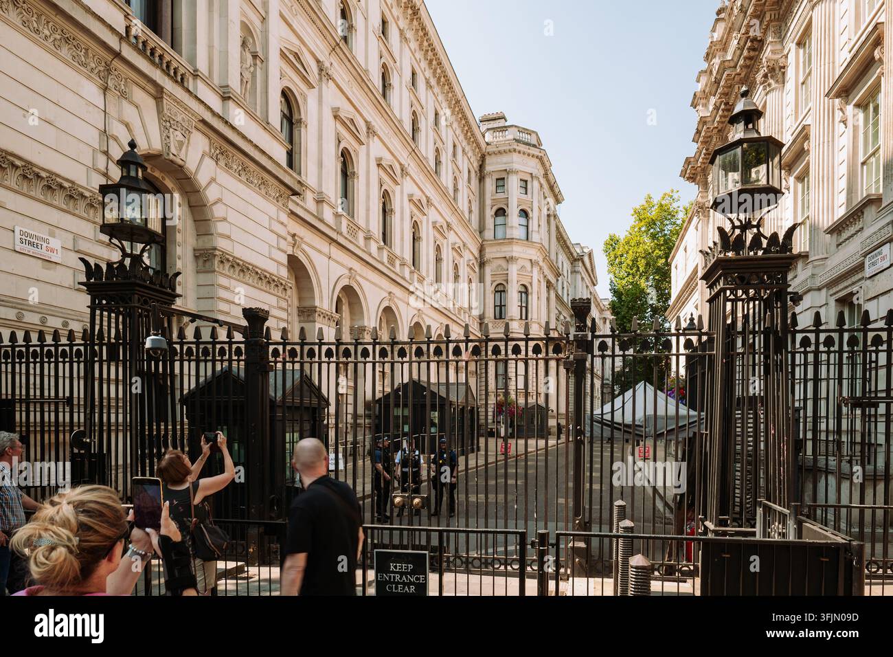 London, England, Vereinigtes Königreich, 14. August 2026. Touristen machen Fotos vor den Sicherheitstoren, die zu Downing Street in Whitehall führen, an einem hellen Sommer Stockfoto